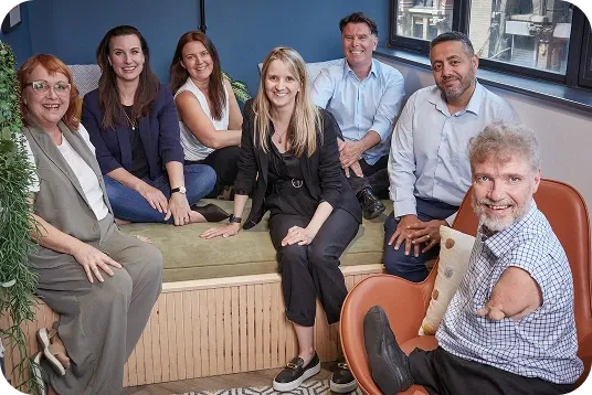 The EnableAll team smiling together on an office bench, with a colleague in a wheelchair in the foreground.